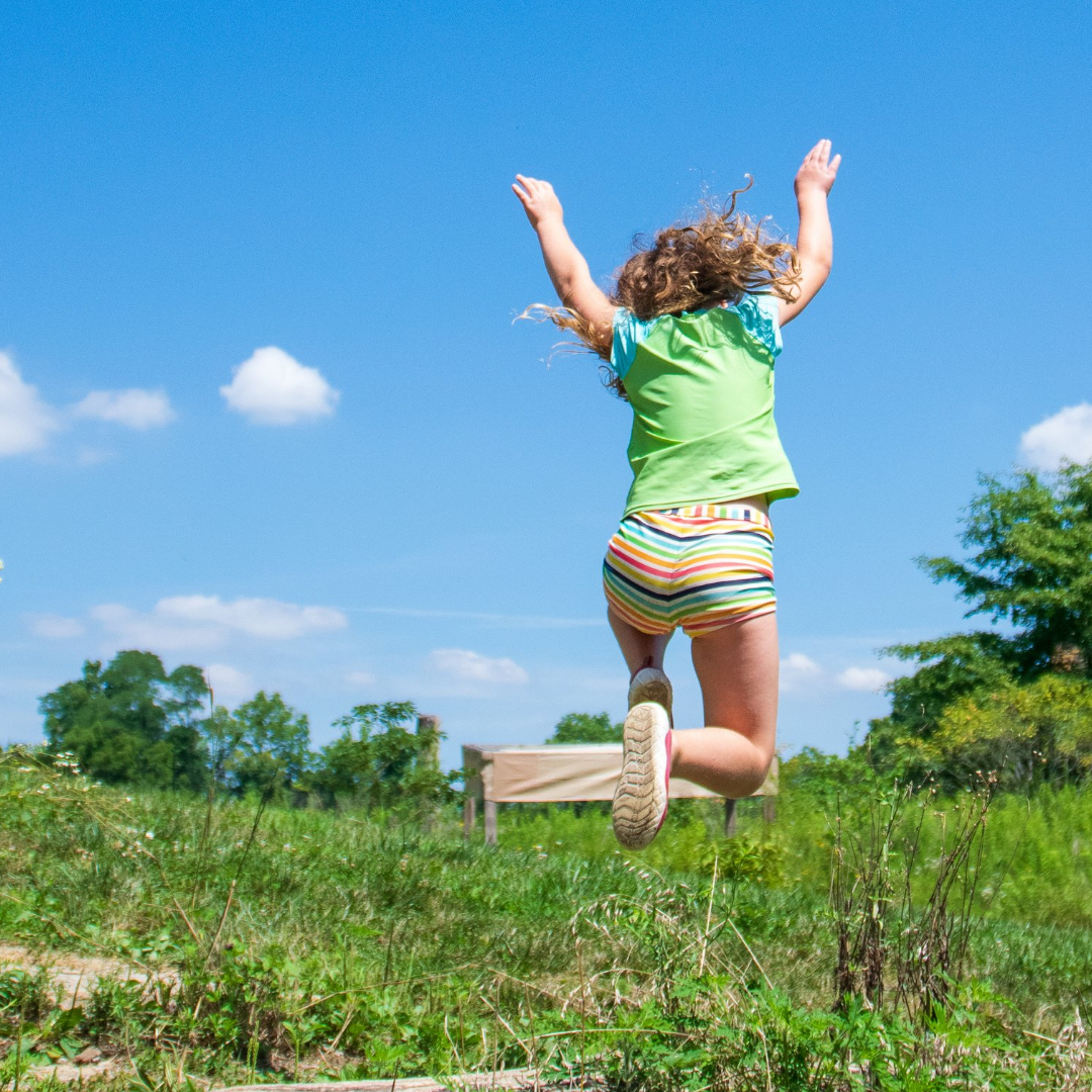 A young girl jumping high against a blue sky